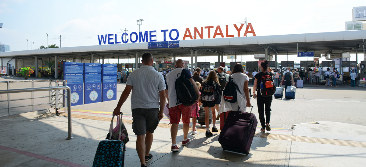 Antalya Havalimanı'ndan çıkan yolcular, valizleriyle birlikte transfer hizmeti için ilerliyor.